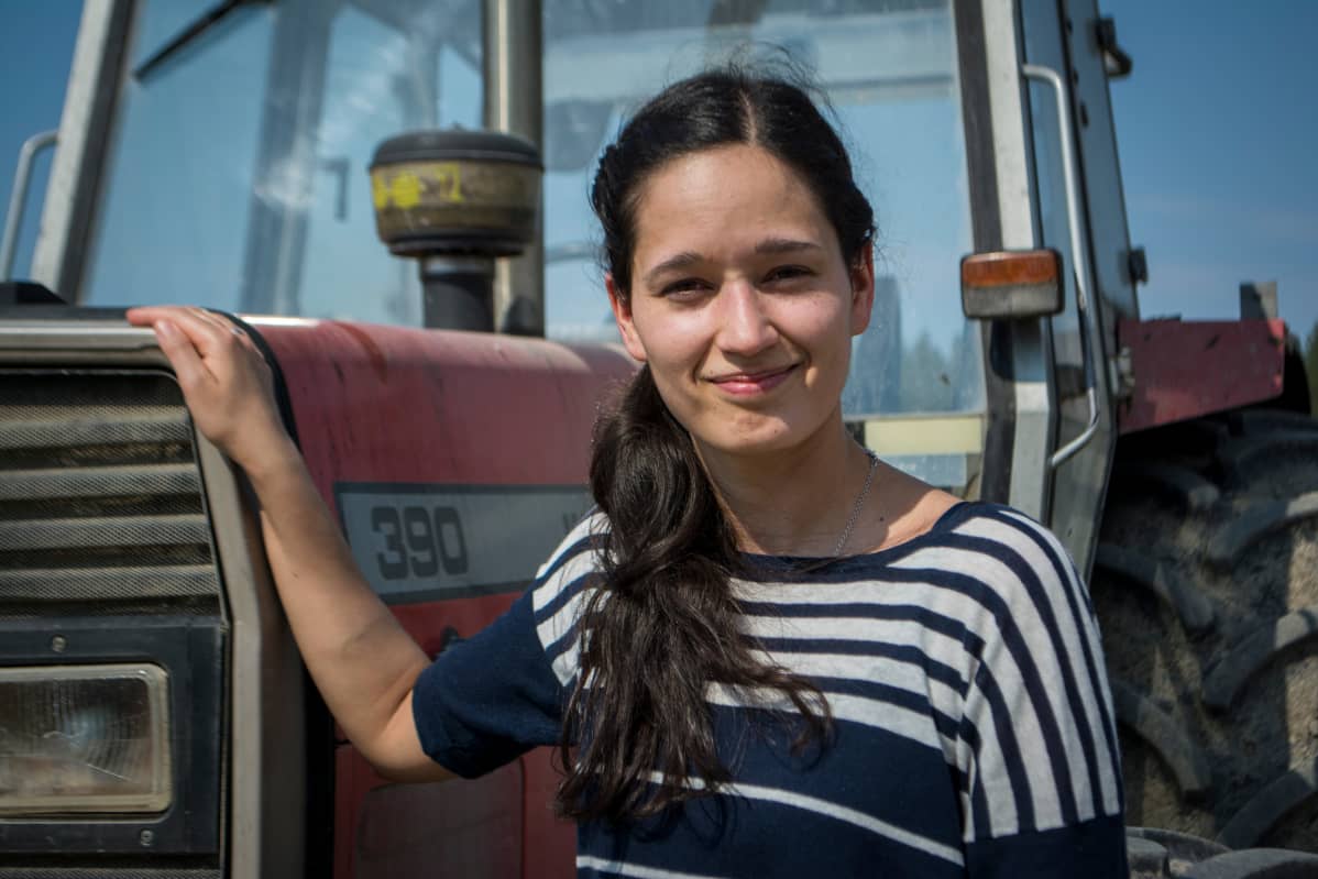 Mikaela seisoo traktorin vieressä maitotilalla.