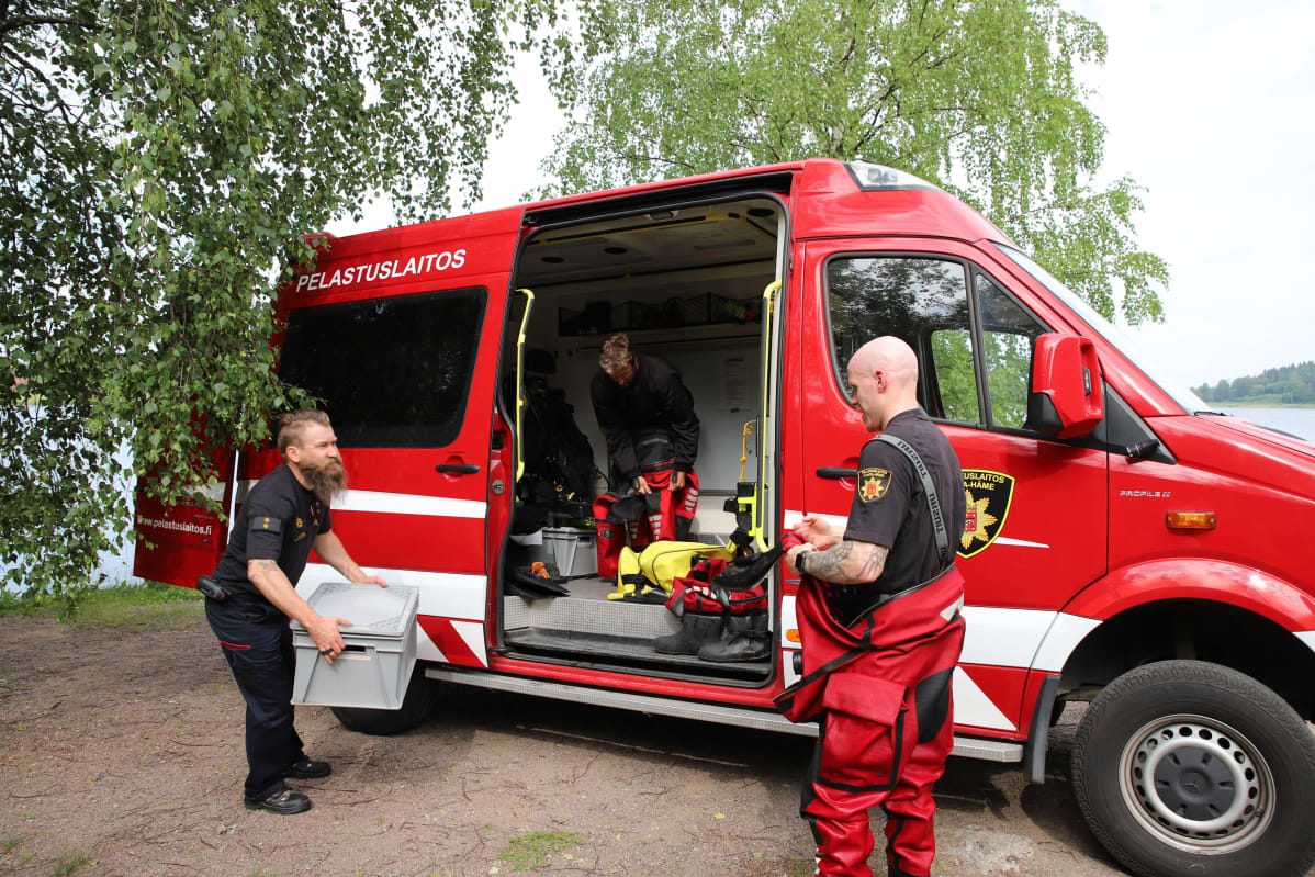 Kolme palomiestä nostaa varusteita pelastuslaitoksen autoon
