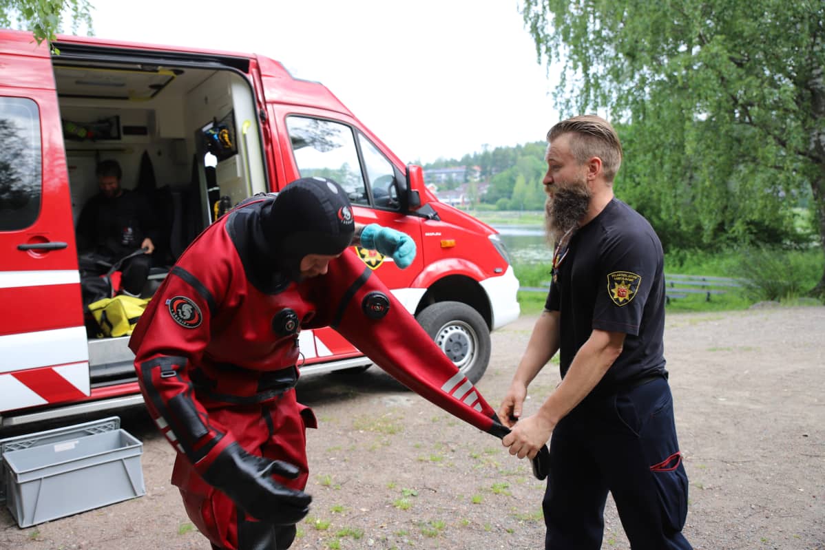 Palomies auttaa sukelluspukua sukeltajan päältä