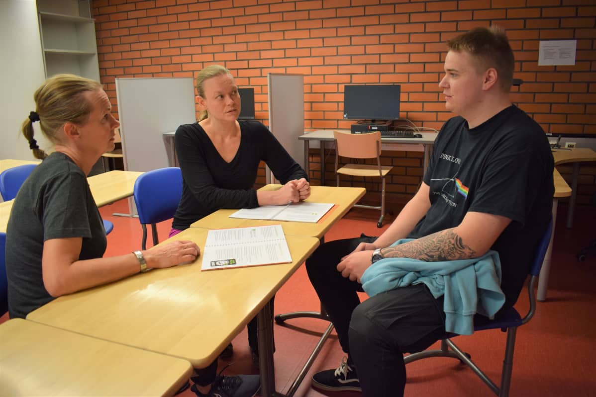Kokkiopiskelija istuu opo ja hanketyöntekijän kanssa pöydän ääressä.