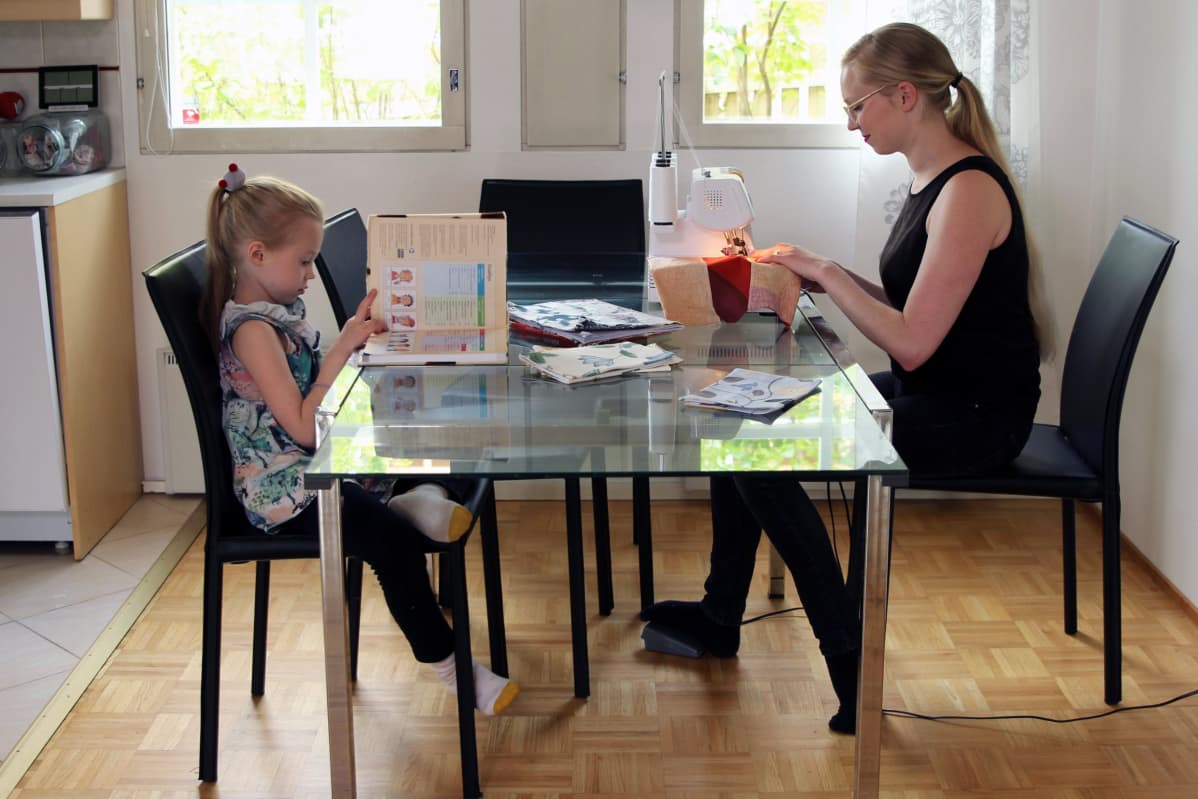 Elsi ja Anni Ignatius keittiön pöydän ääressä. Elsi lukee koulukirjaa, Anni ompelee.