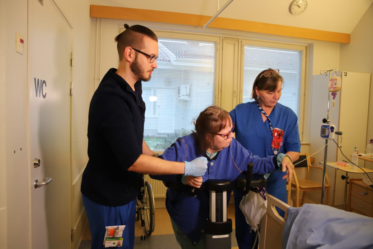 Fysioterapeutti Sami Backman ja sairaanhoitaja Siiri Lapinniemi auttavat potilasta Rovaniemen kuntoutussairaalassa.
