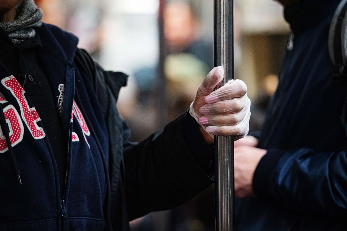 Matkustaja metrossa suojakäsineet kädessä.