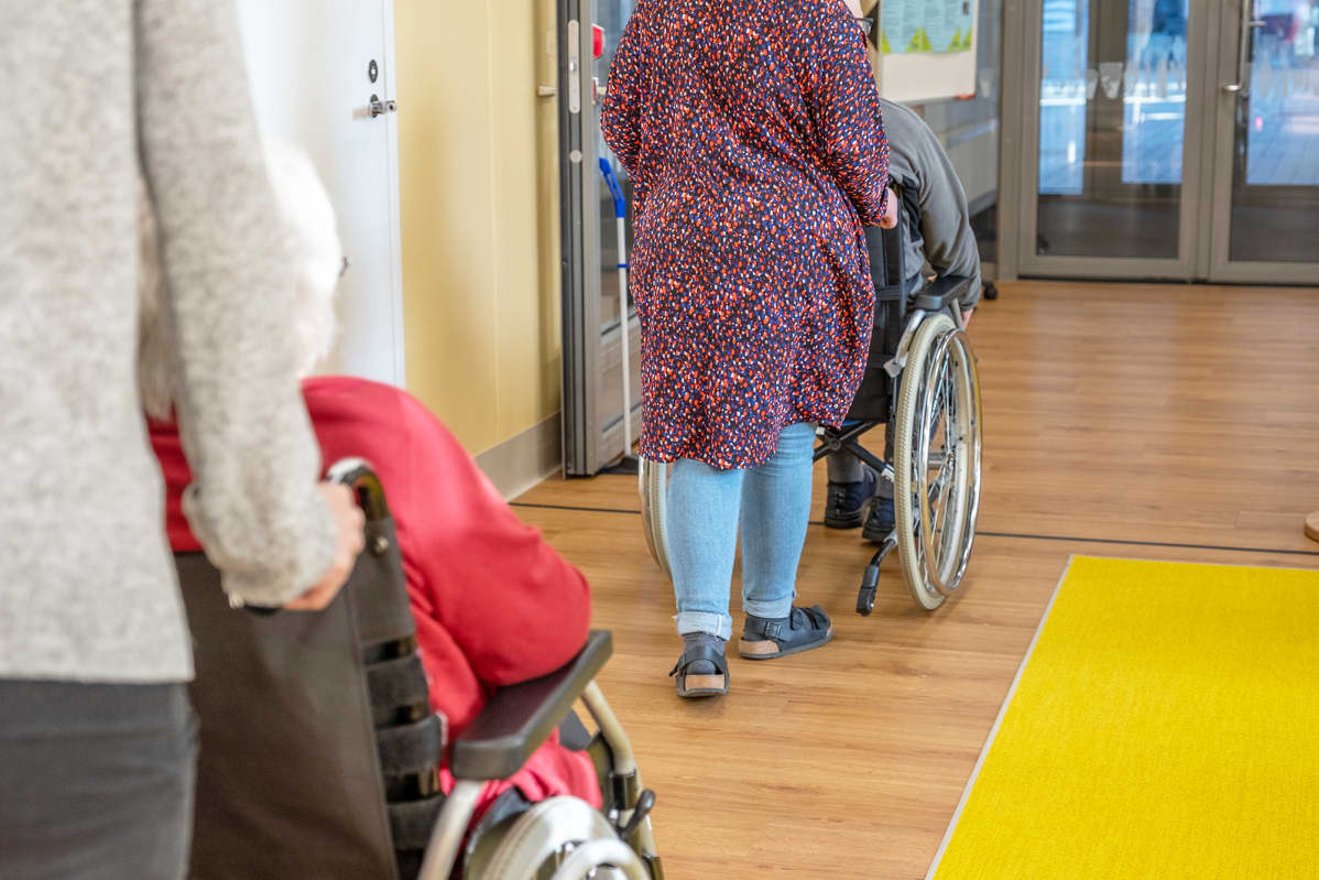Työntekijät työntävät vanhuksia pyörätuolissa vanhustenkeskuksessa.