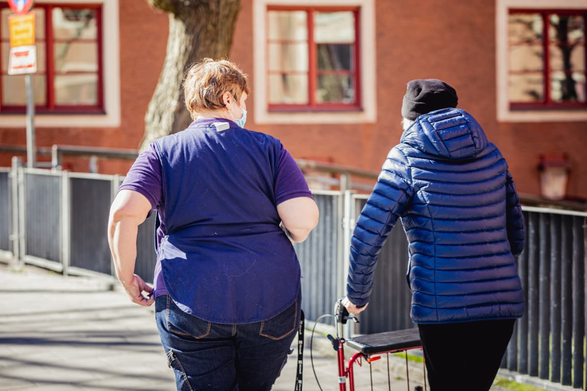 Vanhus rollaattorin kanssa hoitajan kanssa ulkoilemassa.