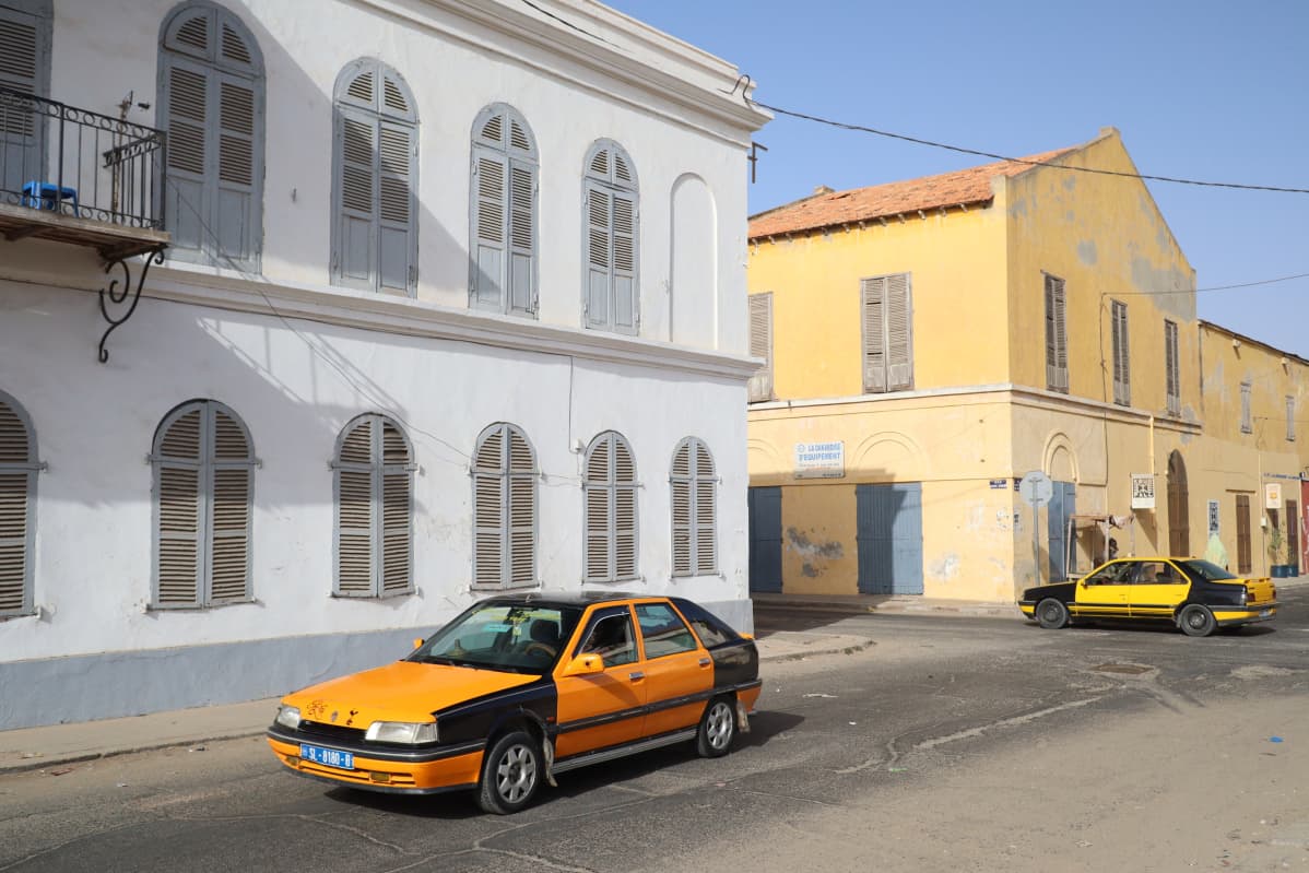 Kaksi siirtomaatyylistä rakennusta ja kaksi keltamustaa autoa Saint-Louis'n vanhankaupungin kaduilla.