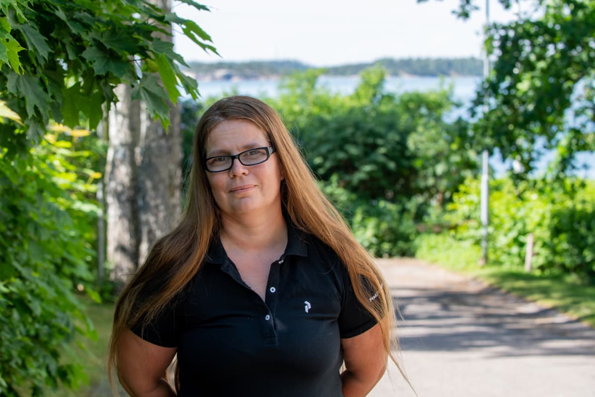 Keski-ikäinen nainen seisoo puistossa takanaan merimaisema.