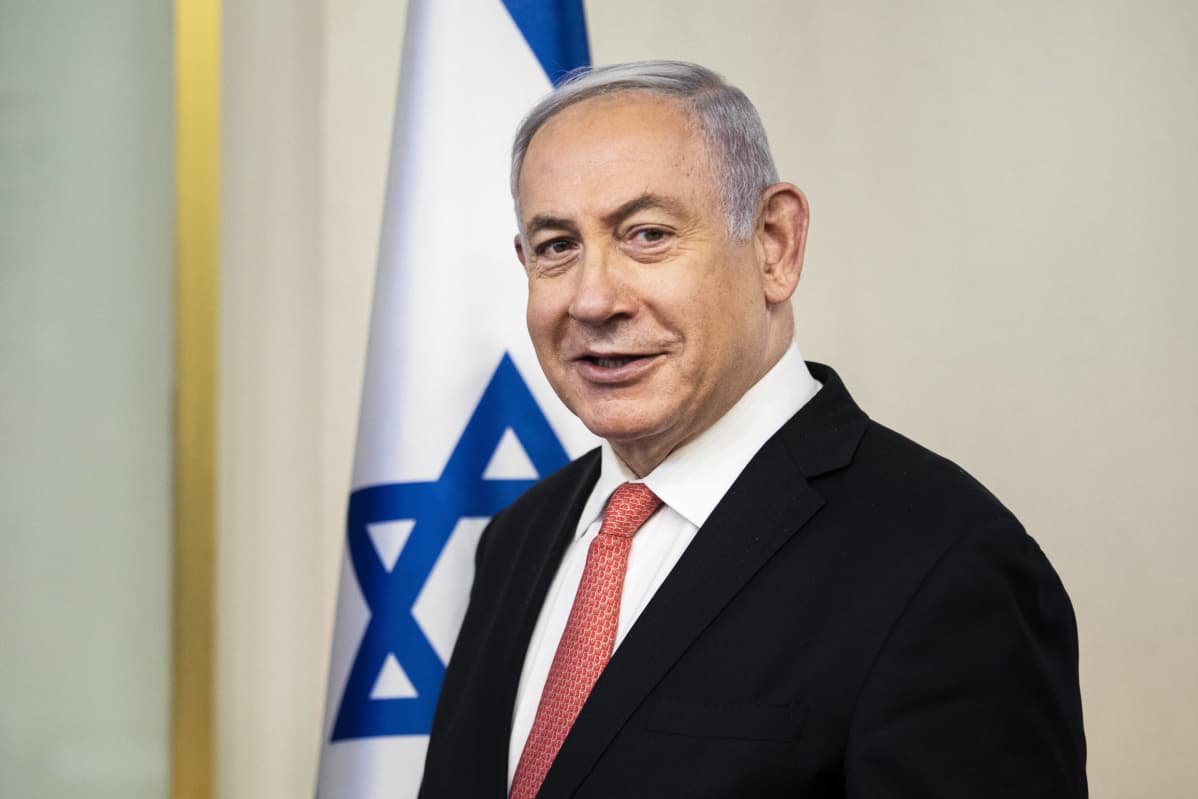 Pääministeri Benjamin Netanjahu katsoo kameraan seisten Israelin lipun edessä.