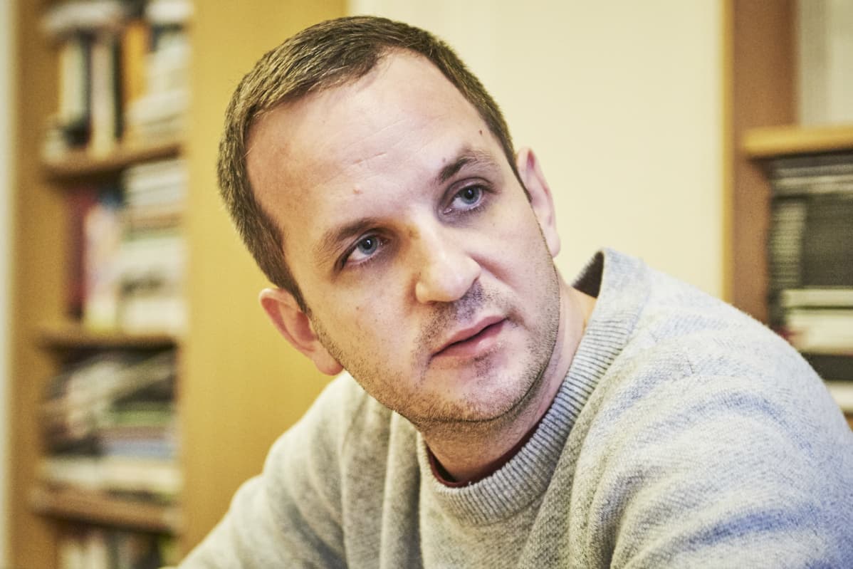 Balázs Tóth harmaassa villapaidassa, taustalla näkyy kirjahyllyjä.