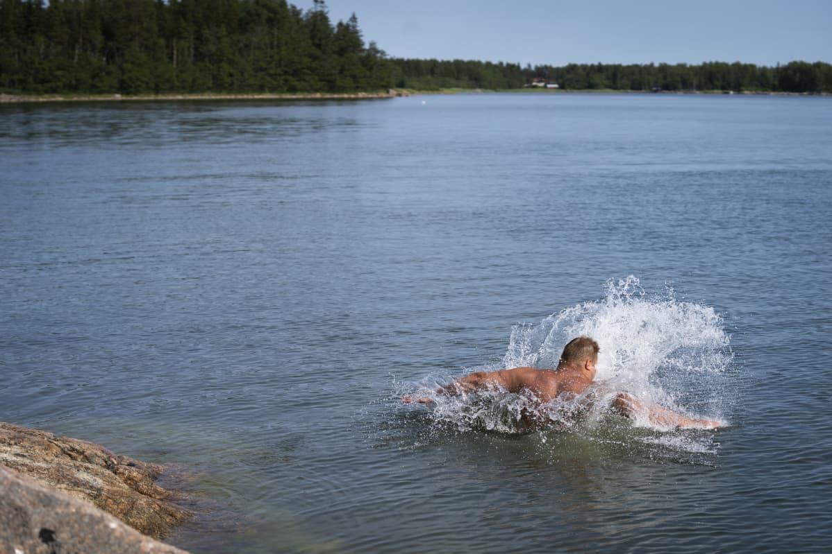 Mies hyppää kalliolta veteen uimaan.