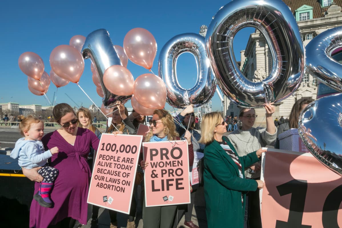 Aborttia vastustavat naiset kantavat kylttejä ja ilmapalloja Pohjois-Irlannin toimiston edustalla helmikuussa 2019. Kyltissä lukee: sata tuhatta ihmistä on elossa aborttilakiemme ansiosta.