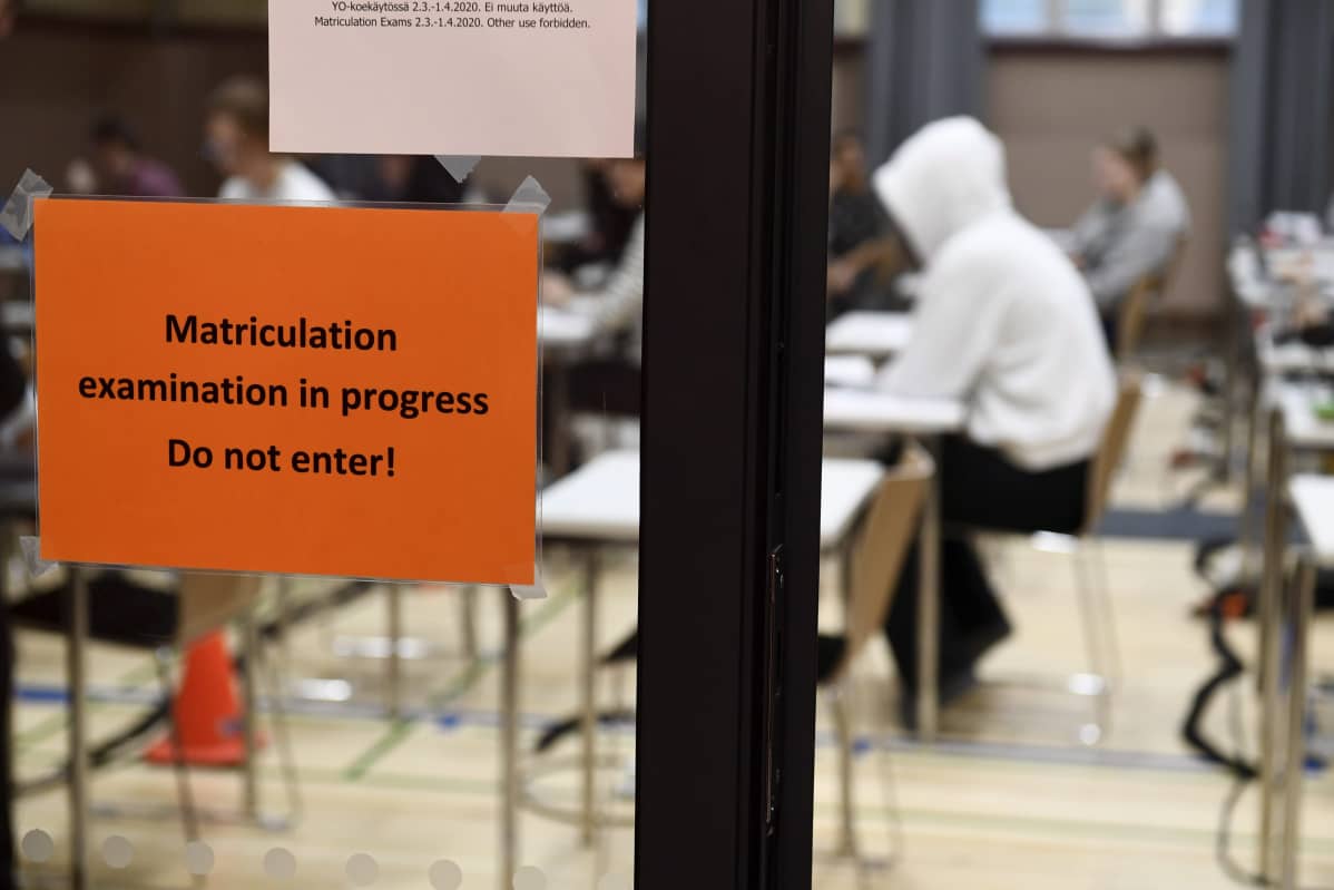 Lapp på glasdörr som säger att man inte får störa eftersom studentskrivningar pågår, ungdomar i bakgrunden
