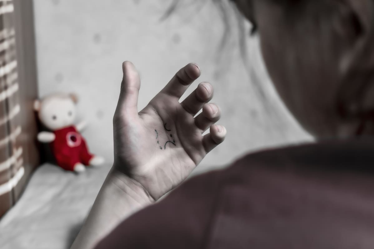 Dramatisoitu kuva, jossa lapsi katselee kämmeneen piirtämäänsä itkevää hymiötä.