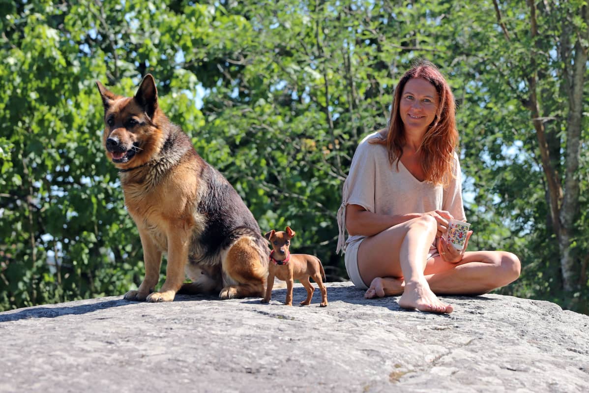 melina Holmberg istuu kalliolla koiriensa kanssa.
