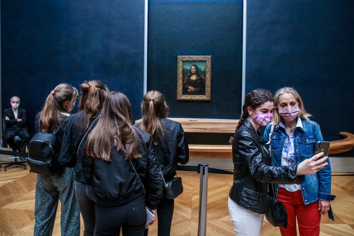 Kaksi selfietä ottavaa naista Mona Lisan edessä.