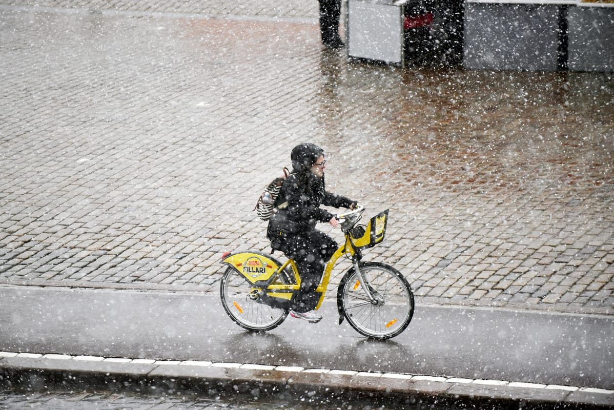 Nainen pyöräilee kaupunkipyörällä lumisateessa Helsingissä.