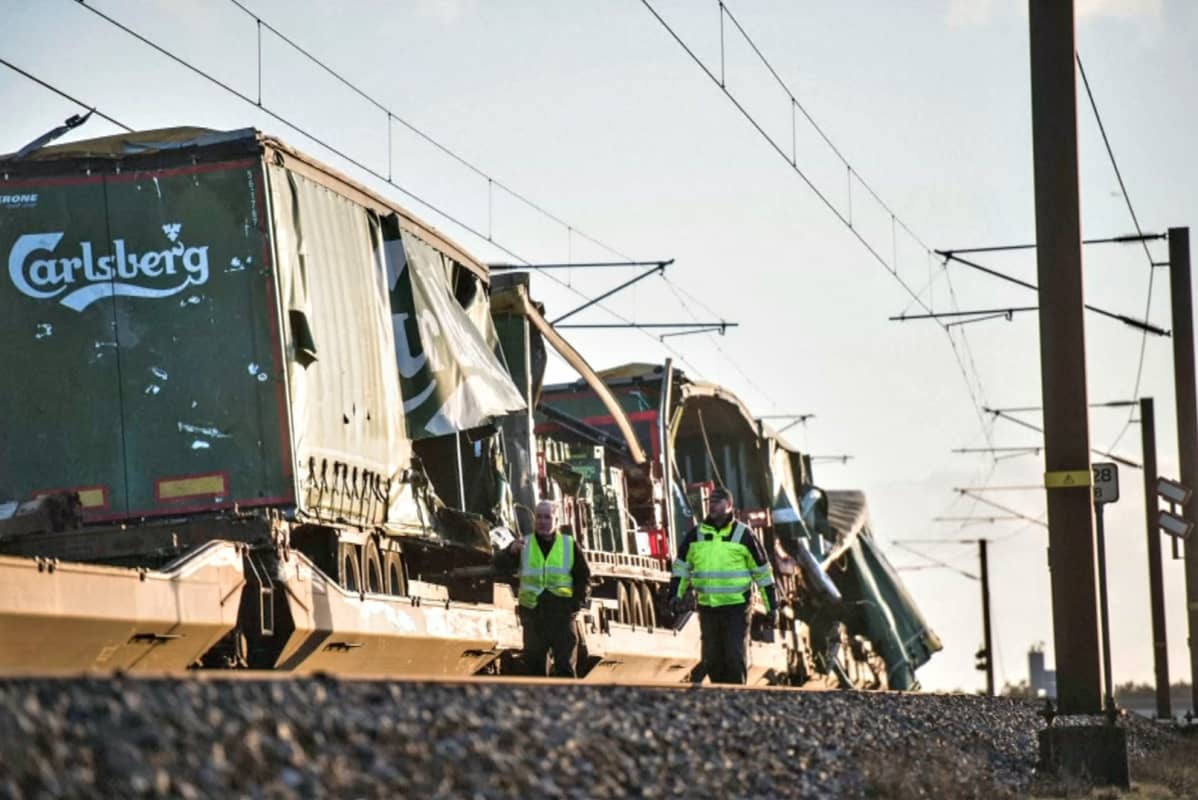 Tavarajuna on jäänyt pysähdyksiin Ison-Beltin sillalle. Kaksi keltaliivistä miestä kävelee rikkoutuneen tavarajunan kontin ohitse.