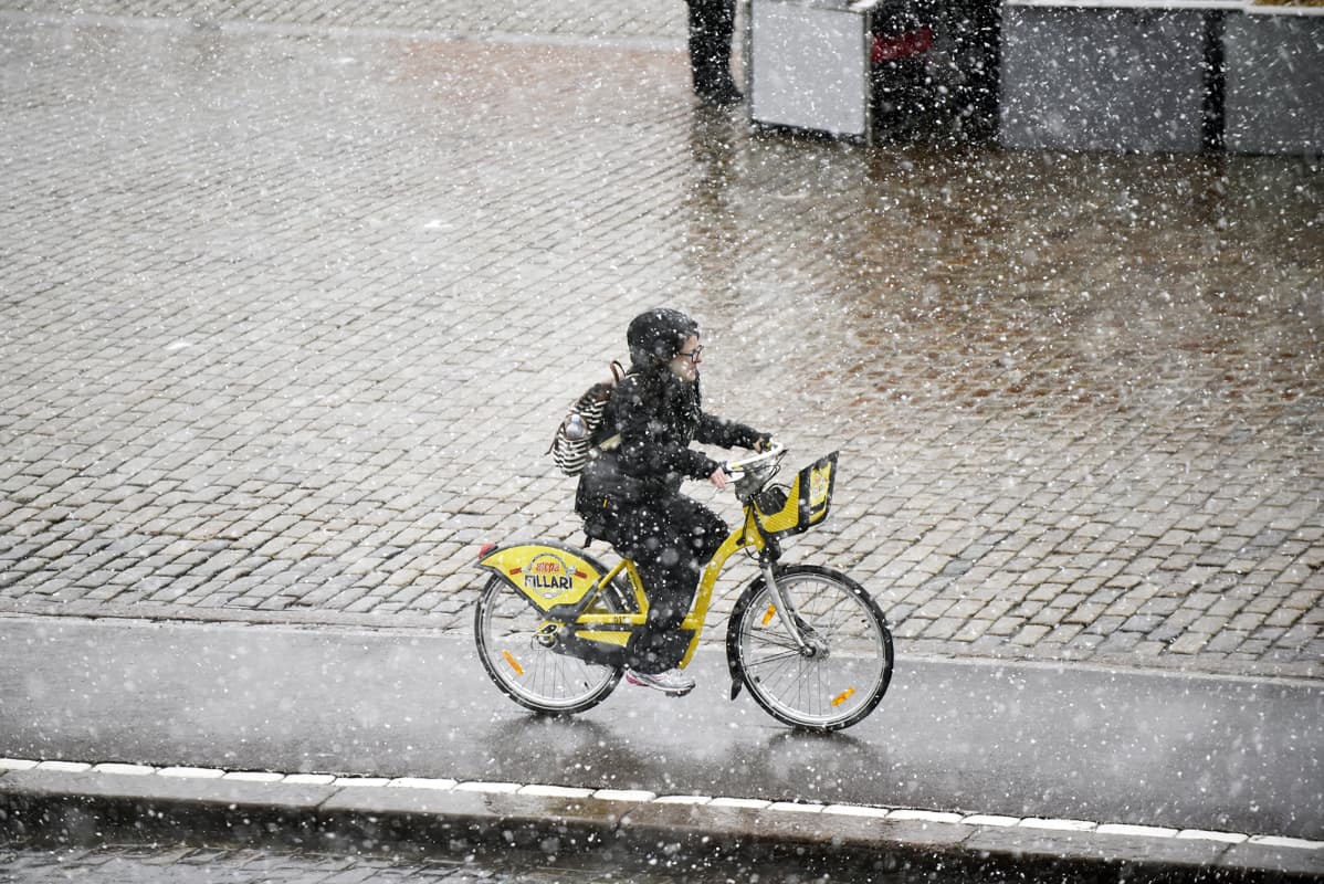 Nainen pyöräilee kaupunkipyörällä lumisateessa Helsingissä.