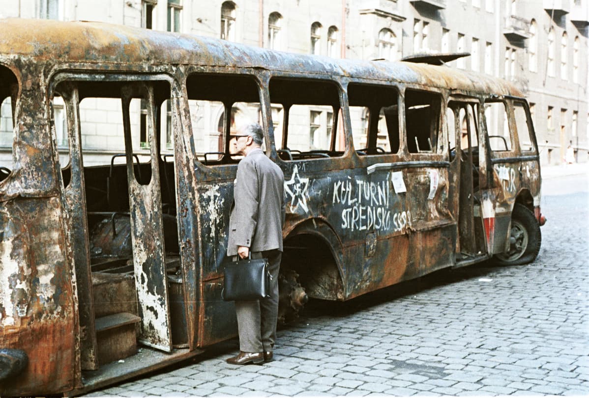 Prahalaismies tarkastelee neuvostovastaisilla iskulauseilla maalattua palaneen bussin hylkyä.