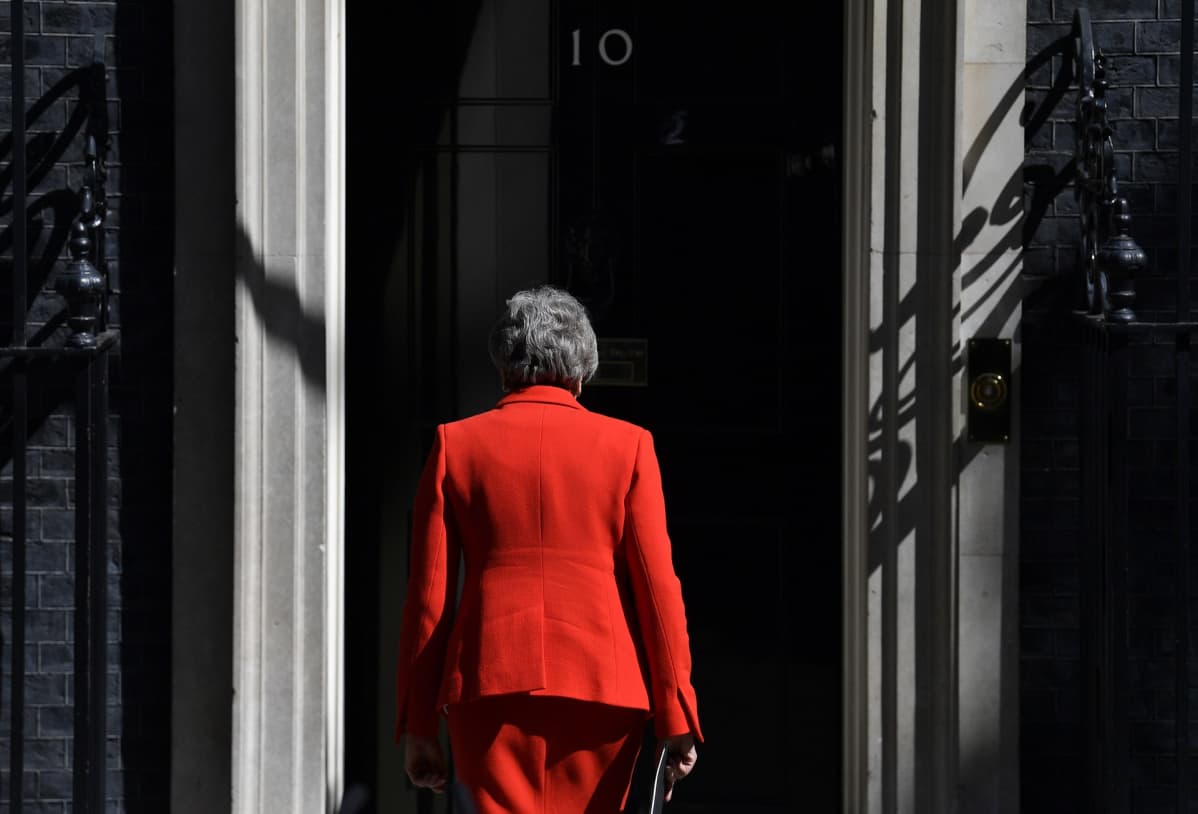 Theresa May kävelee kohti ovea selkä kameraan päin.