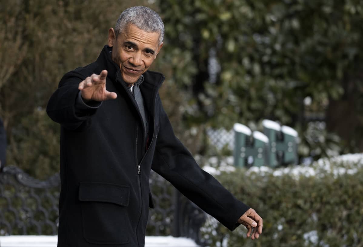 Barack Obama katsoo kameraan ja nostaa kättä tervehdykseksi.