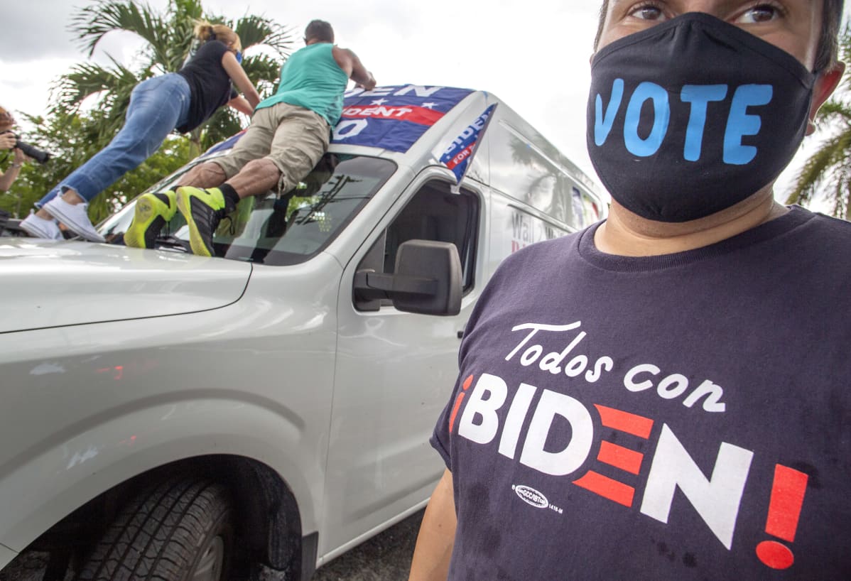 Joe Bidenia kannattavia latinoita Miamissa. Etualalla olevalla naisella lukee paidassa espanjaksi Todos con Biden! Naisen kasvomaskissa lukee englanniksi Vote.