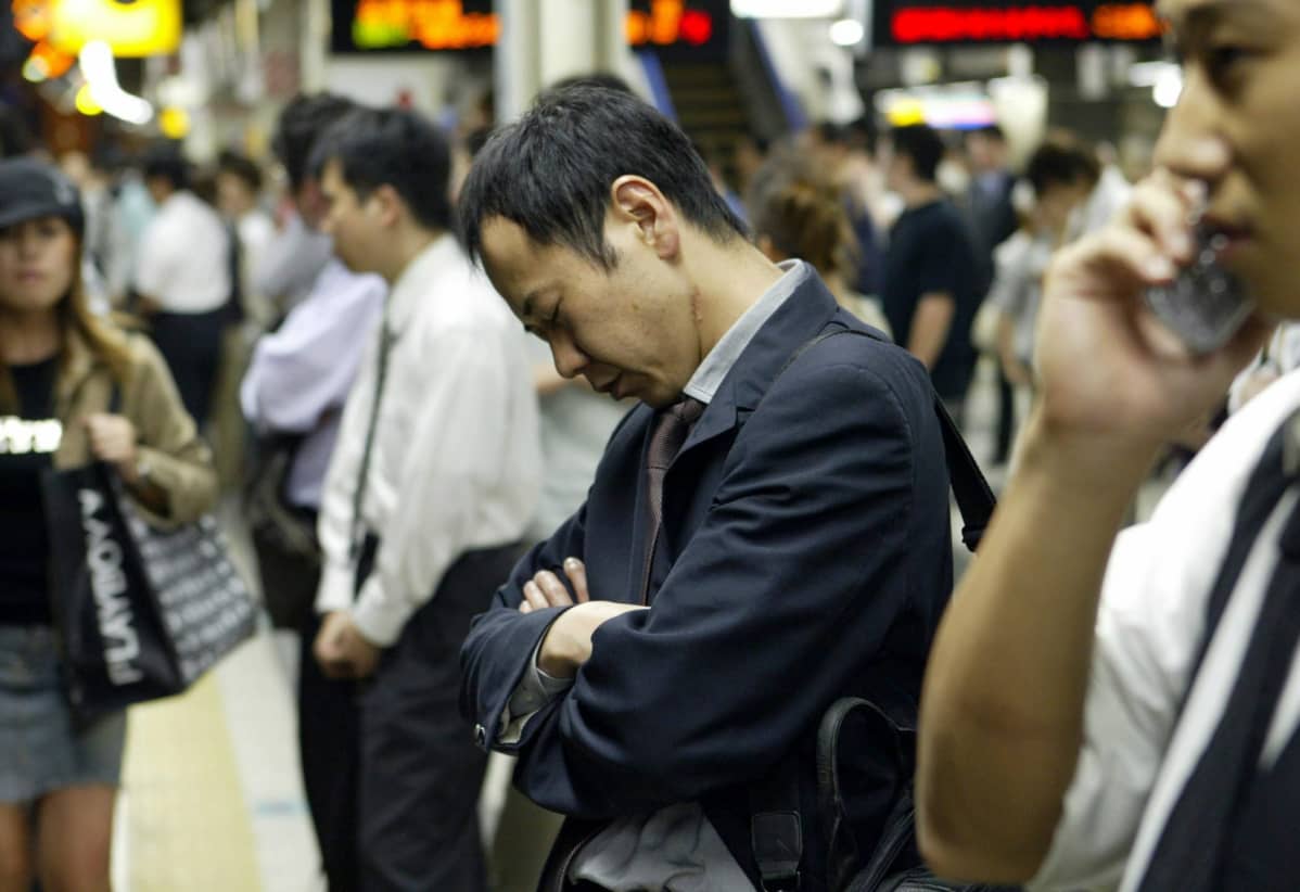 Japanilaismies seisoo silmät kiinni ja pää painuksissa odottamassa junaa.