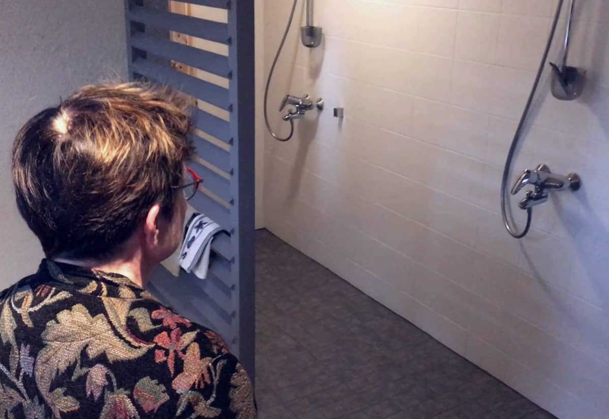 Nainen katselee valkoista pesuhuonetta, jossa on kaksi suihkua.