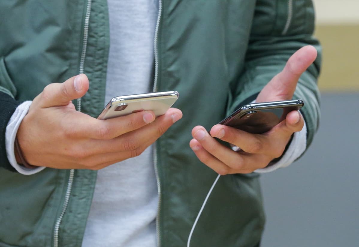 Miehen käsissä iPhone-kännykät.