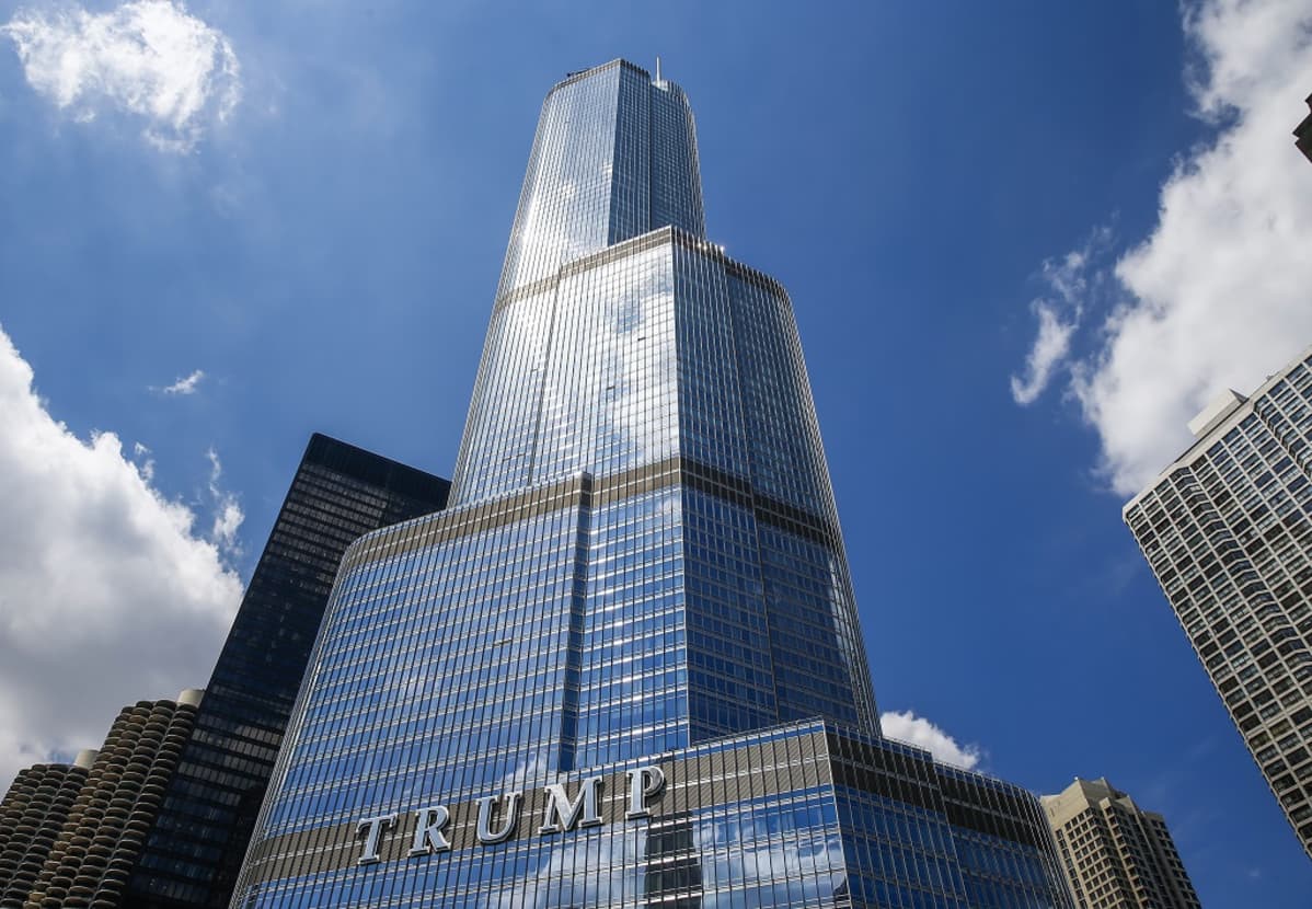 Pilvenpiirtäjä kohoaa korkeuksiin. Tornissa lukee isoin kirjaimin TRUMP. Taivas on melko pilvetön.