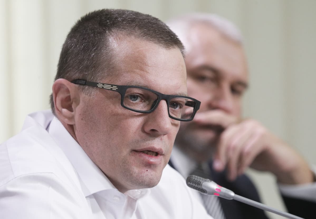 Roman Suštšenko pitää lehdistötilaisuutta Kiovassa 11. syyskuuta 2019. Hänellä on valkoinen kauluspaita ja mustasankaiset silmälasit. Hiukset on leikattu lyhyiksi. Taustalla näkyy sumeana valkotukkainen mies, joka kuuntelee, kun Suštšenko puhuu.