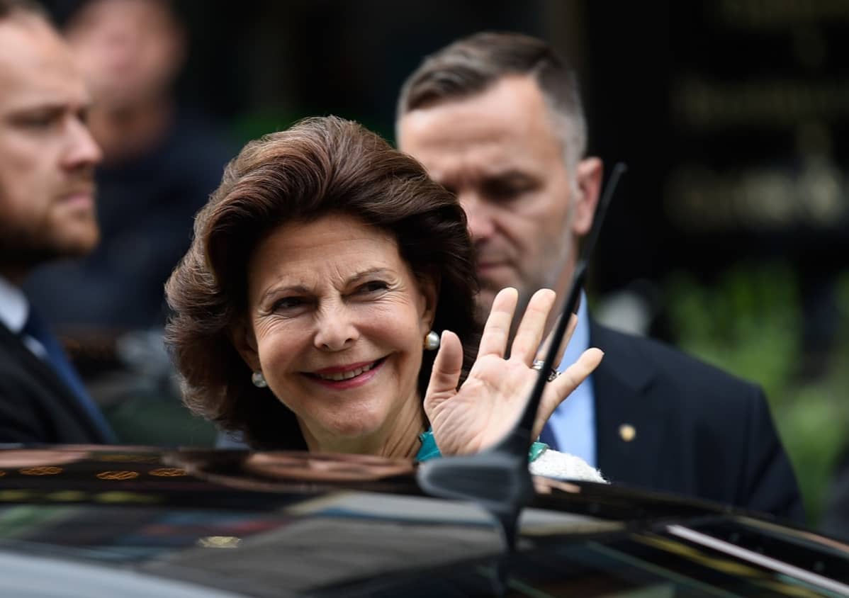 Silvia vilkuttaa lehdistölle, taustalla kaksi turvamiestä.