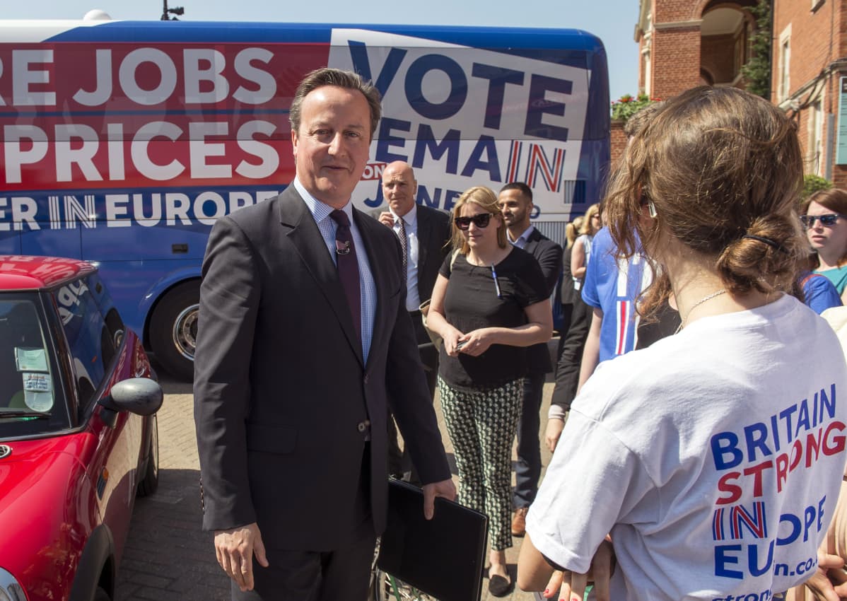 Britannian pääministeri David Cameron ihmisten ympäröimänä, taustallaan bussi, jonka kyljessä lukee "VOTE REMAIN".