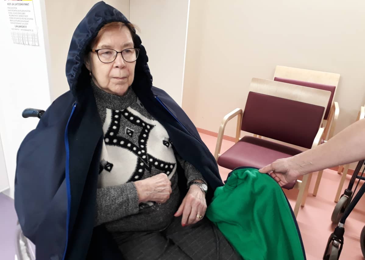 Mirja Malmille puetaan tummansinistä, hupullista ulkoiluviittaa Elimäkikodissa.