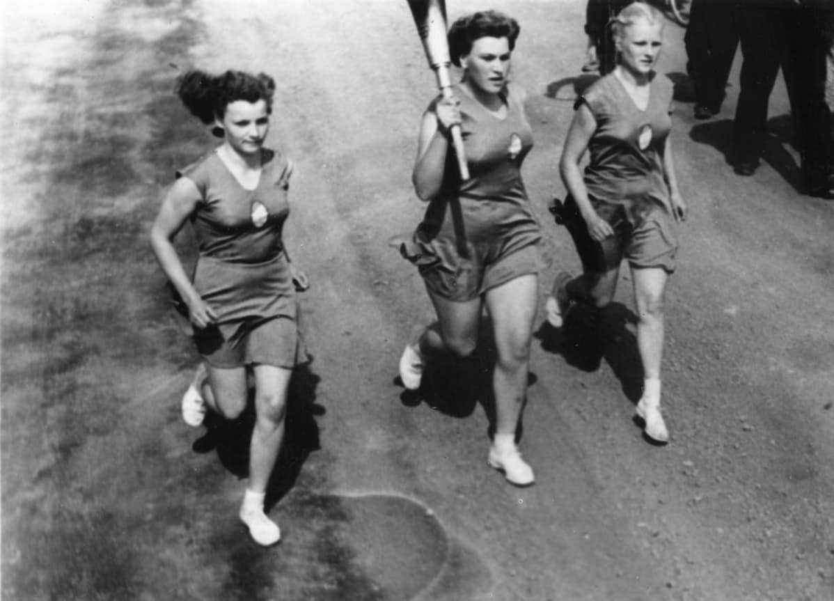 Soihtuviesti Saloisissa 11.7.1952. Soihdunkantaja ja kaksi saattajaa juoksevat maantiellä.
