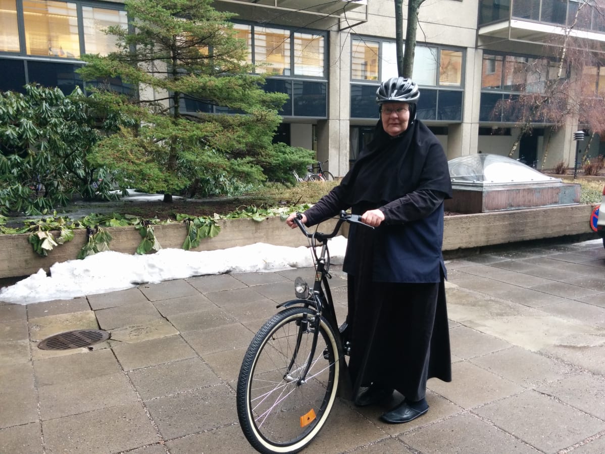Nunna Elisabet kotitalonsa sisäpihalla Mikonkadulla mustan Helkama Aino-merkkisen pyörän kanssa. Taustalla näkyy viherkasveja ja kerrostalon seinää.