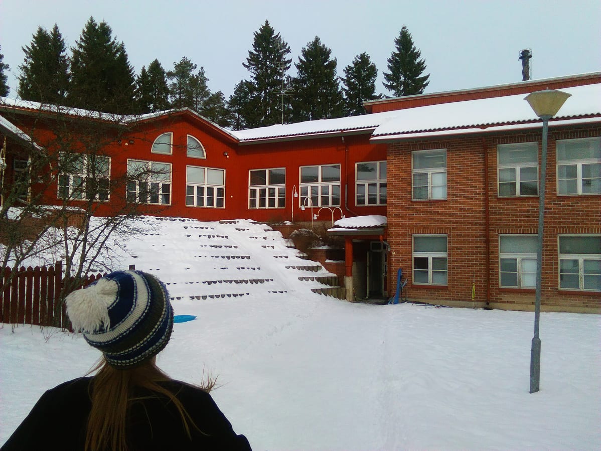 Kuvassa punatiilinen koulu ja oppilas, joka on matkalla kouluun.