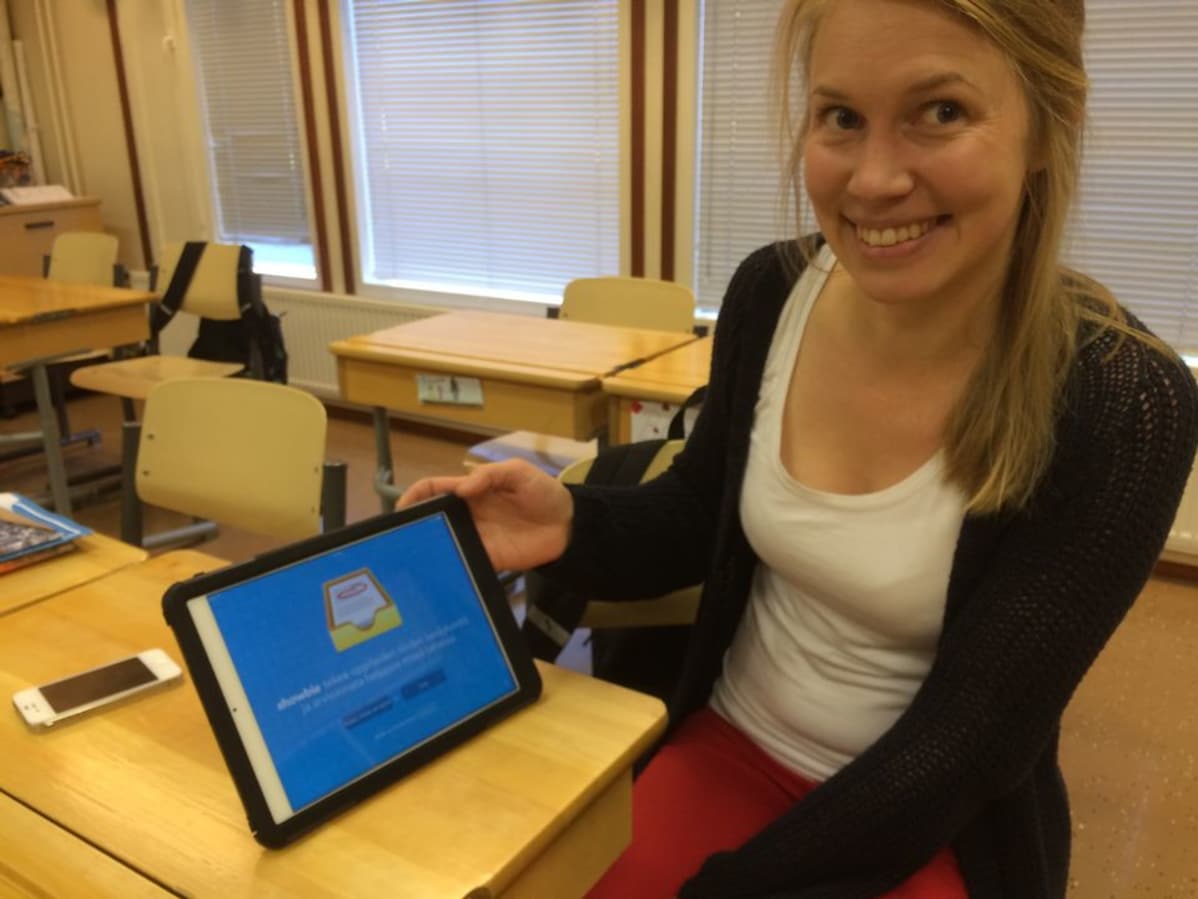 Johanna Laitila esittelee tablettia. Vierellä on myös älypuhelin.