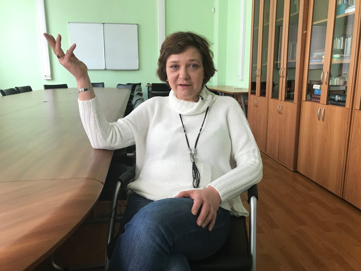 Jelena Panfilova istuu ja nostaa oikeaa kättään ilmaan katsoen kameraan.