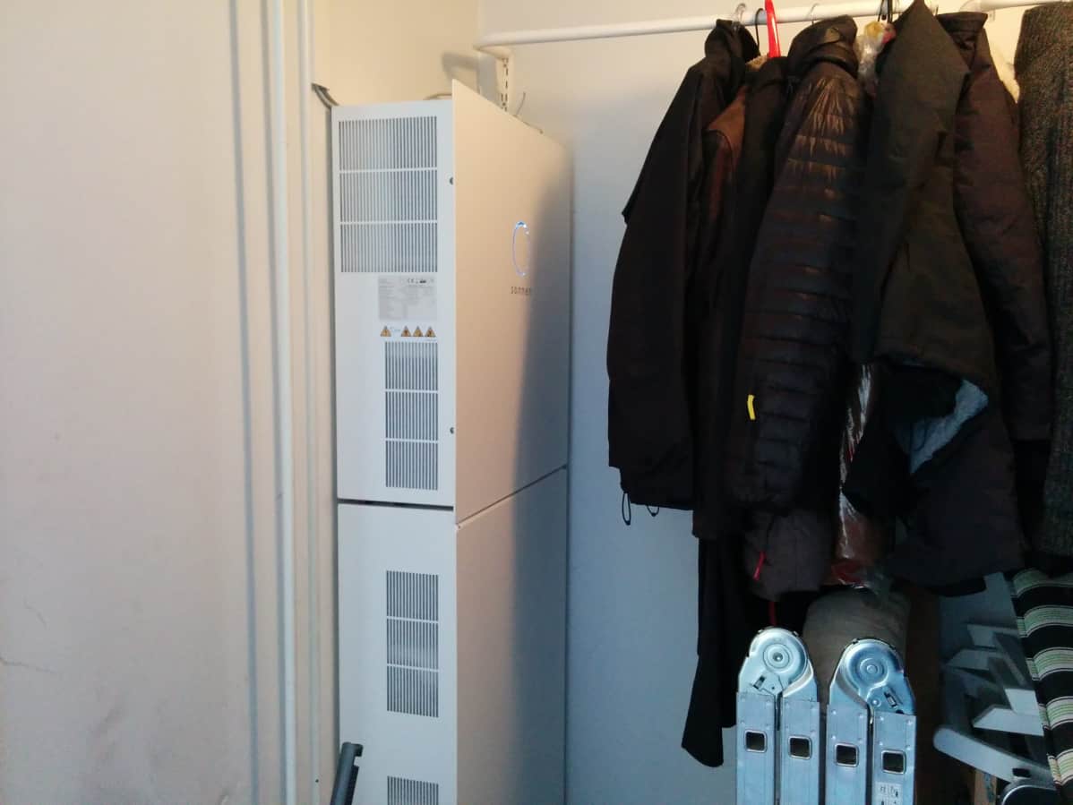 Sähkövaraston valkoiset laatikon muotoiset akut on sijoitettu lämpimän ulkovaraston nurkkaan vaaterekin viereen.