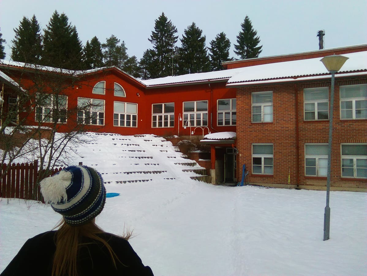 Kuvassa punatiilinen koulu ja oppilas, joka on matkalla kouluun.