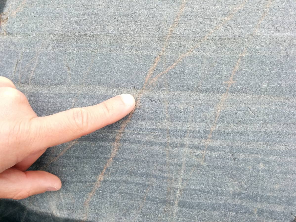 Heinonen näyttää sormella kallion pinnassa olevia kerroksia, jotka kertovat muinaisista tulivuorenpurkauksista.