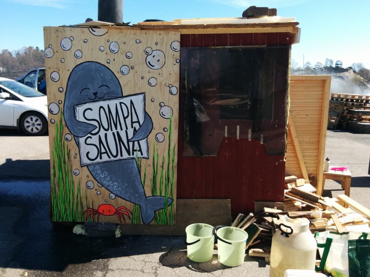 Maalauksessa hylje pitää sylissään kylttiä, jossa lukee "Sompasauna"