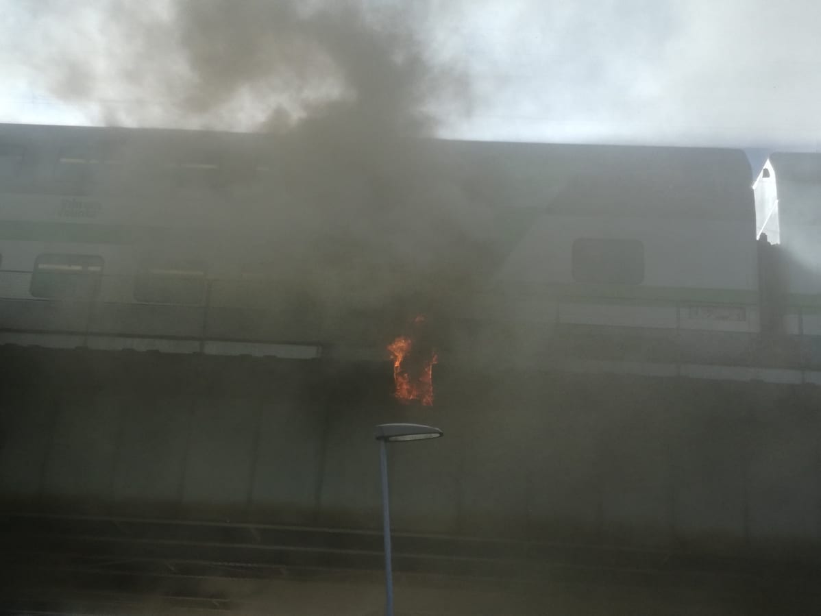 Tulipalopaikan päällä seisova matkustajajuna on savun peitossa.