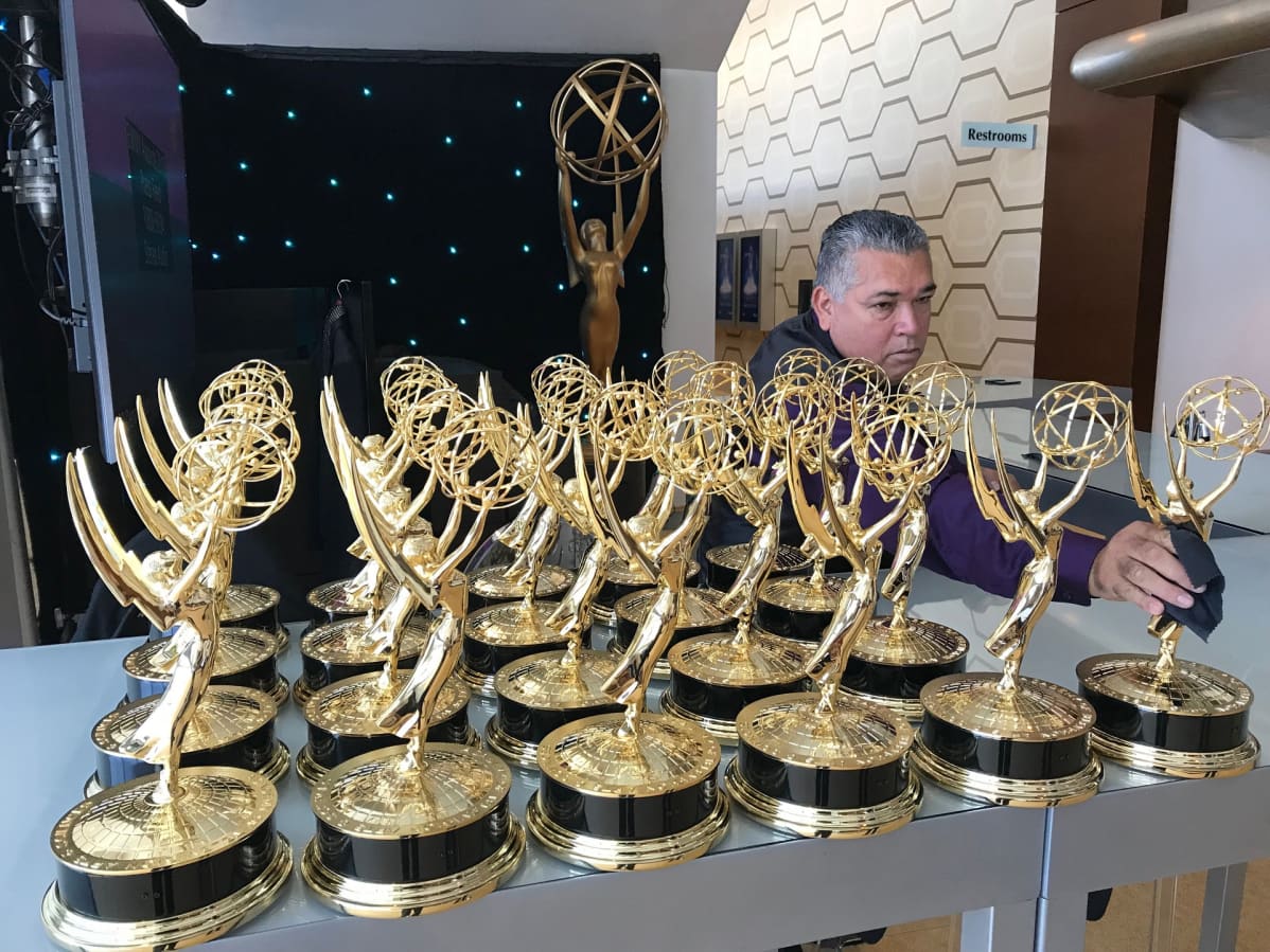 Emmy-pystejä rivissä pöydällä odottamassa palkintojen luovuttamista. Työntekijä järjestää niitä riviin paikalleen.