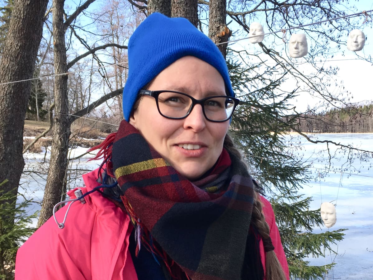 Kuvataiteilija Heidi Piippo ja taustalla roikkumassa valkoisia naamioita paikassa, jossa aikanaan noustiin maihin matkattaessa vesitse kirkolla.