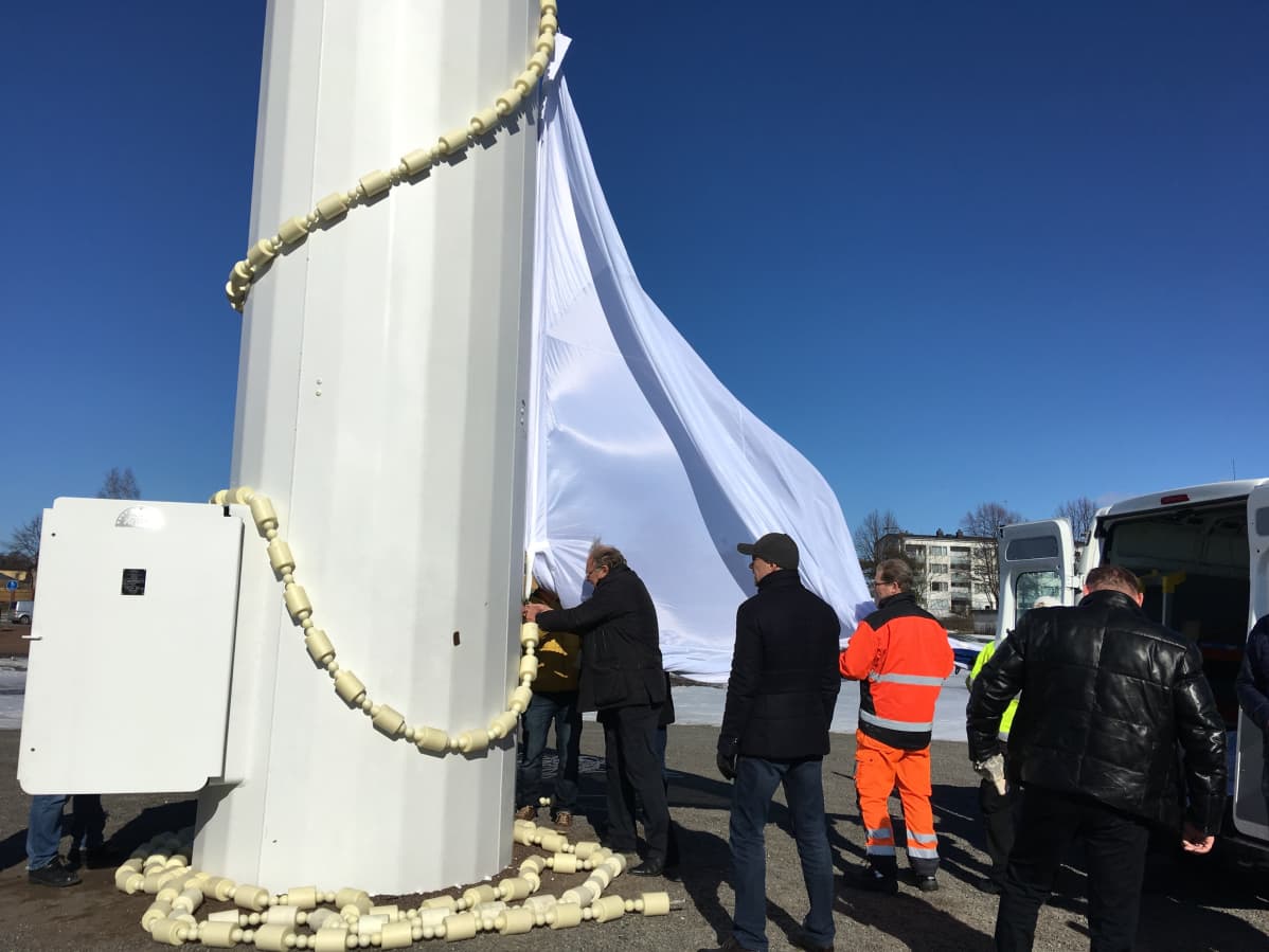 Valkoista kangasta kiinnitetään ensimmäistä kertaa satametrisen lipputangon juurella teräsvaijeriin.