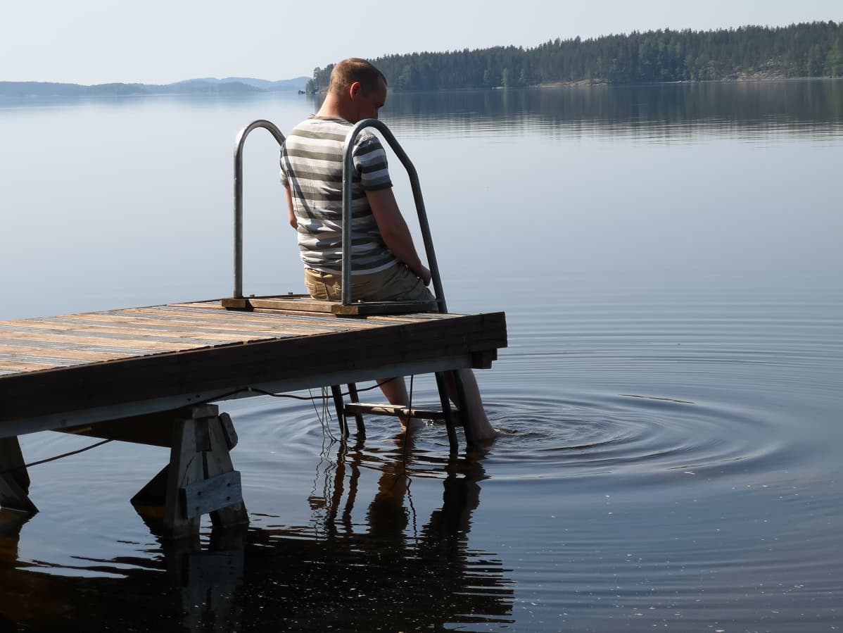 Mies istuu laiturinnokassa Puumalassa.