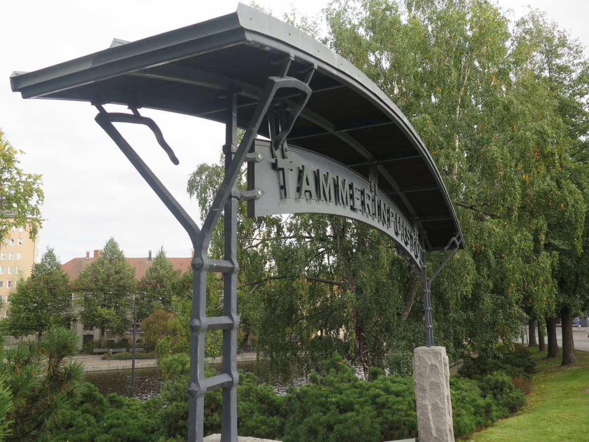 Raudasta taottu kaareva Tammerinpuiston portti nimikyltteineen Tampereen keskustassa.