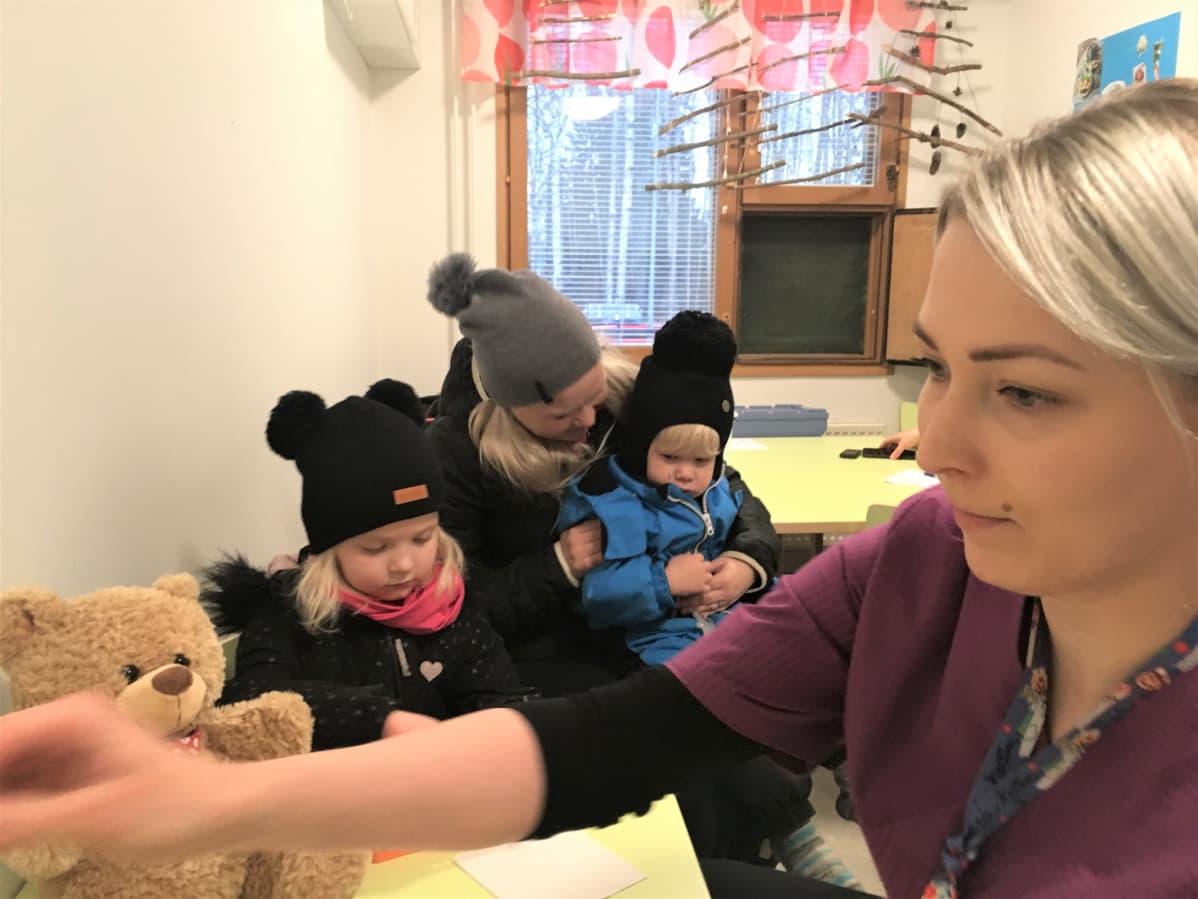 Terveydenhoitaja Siiri Vuorinen valmistelee influenssarokotteita päiväkodissa. Pinja, Emmi ja Perttu Hirvonen odottavat vuoroaan.